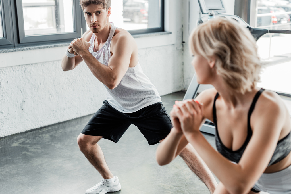 selective focus of young sport couple with clenched hands looking at each other and exercising in gym  - Photo, Image