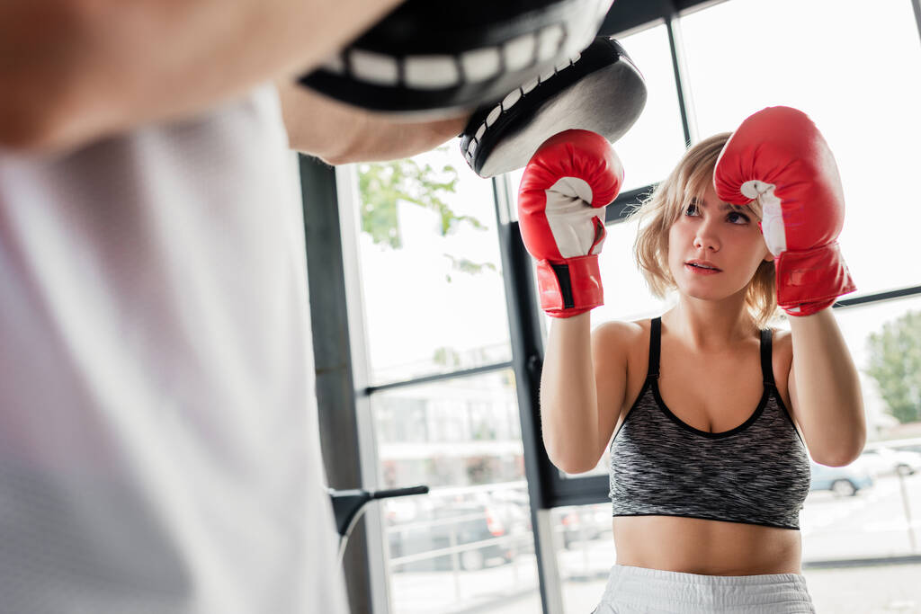 ボクシングパッドの男と運動するボクシンググローブのスポーツ女性の選択的な焦点  - 写真・画像