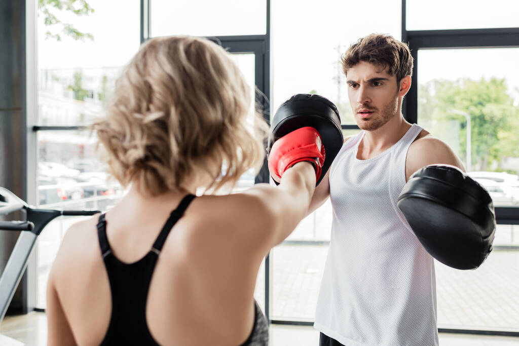 vista posterior de la mujer deportiva en guantes de boxeo haciendo ejercicio con el hombre en almohadillas de boxeo
  - Foto, imagen