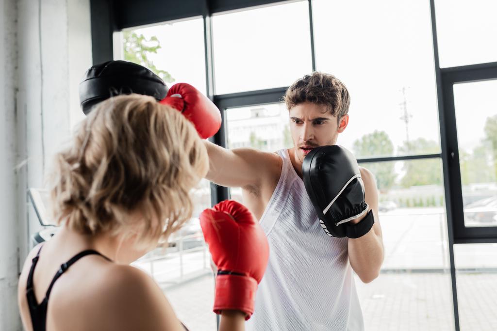 selektiver Fokus des Sportpaares in Boxhandschuhen und Polstern beim Training im Fitnessstudio  - Foto, Bild