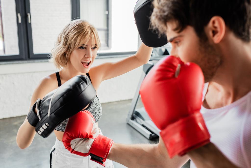 selective focus of emotional sportswoman in boxing pads exercising with man in gym  - Photo, Image