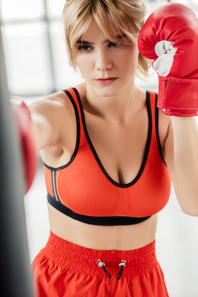パンチングバッグで運動するボクシンググローブのスポーツ女性の選択的な焦点  - 写真・画像