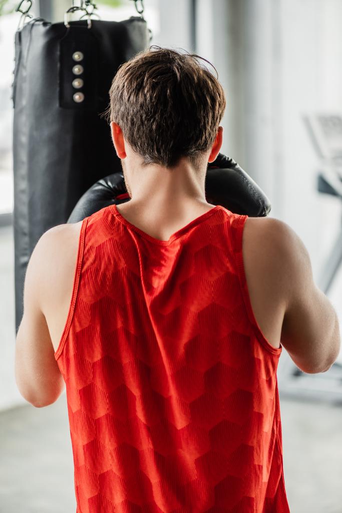 visão traseira do homem atlético em roupas esportivas e luvas de boxe trabalhando com saco de perfuração
  - Foto, Imagem