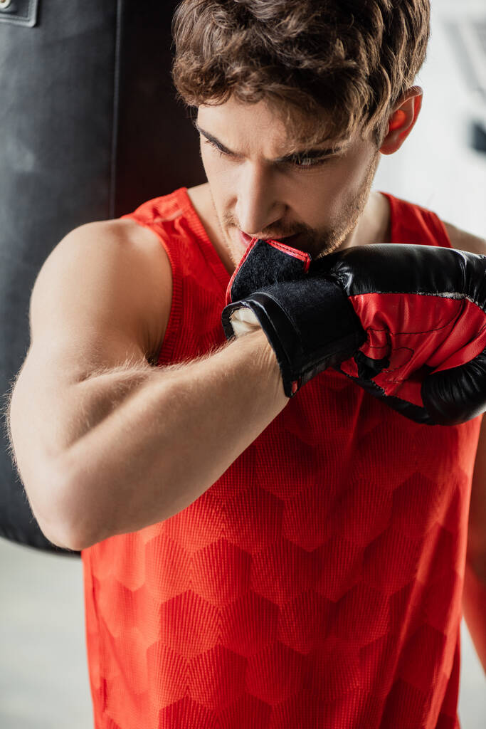 Sportler in Sportbekleidung beißt Boxhandschuh im Fitnessstudio  - Foto, Bild
