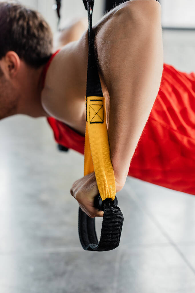 oříznutý pohled na silného muže cvičícího s elastikou v tělocvičně  - Fotografie, Obrázek
