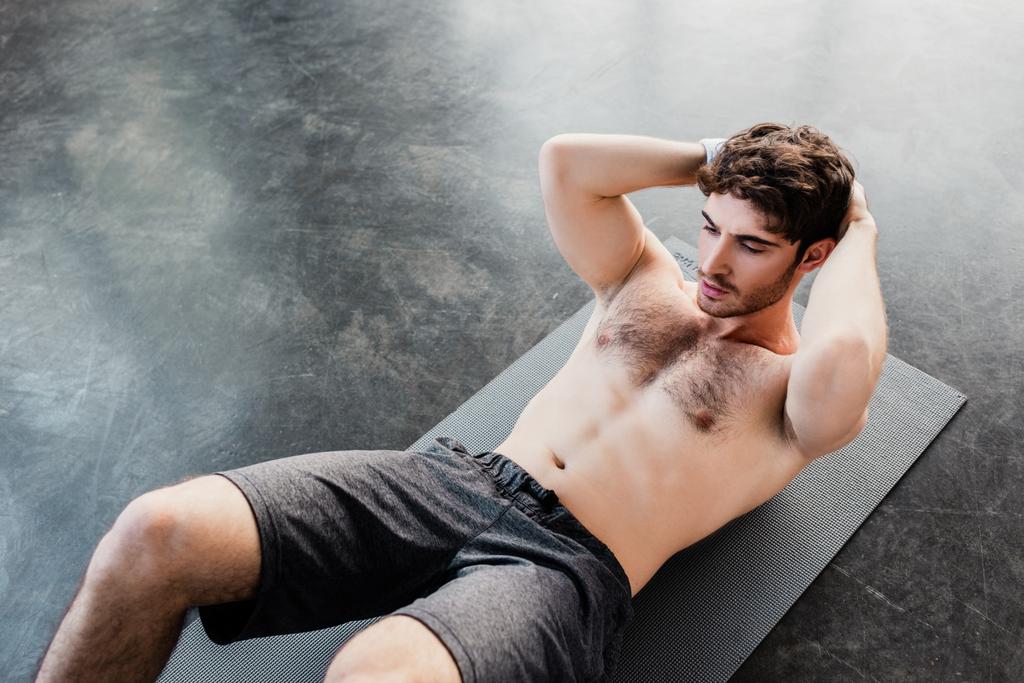 vista de ángulo alto de deportista guapo haciendo sentadas en la alfombra de fitness en el gimnasio
  - Foto, imagen