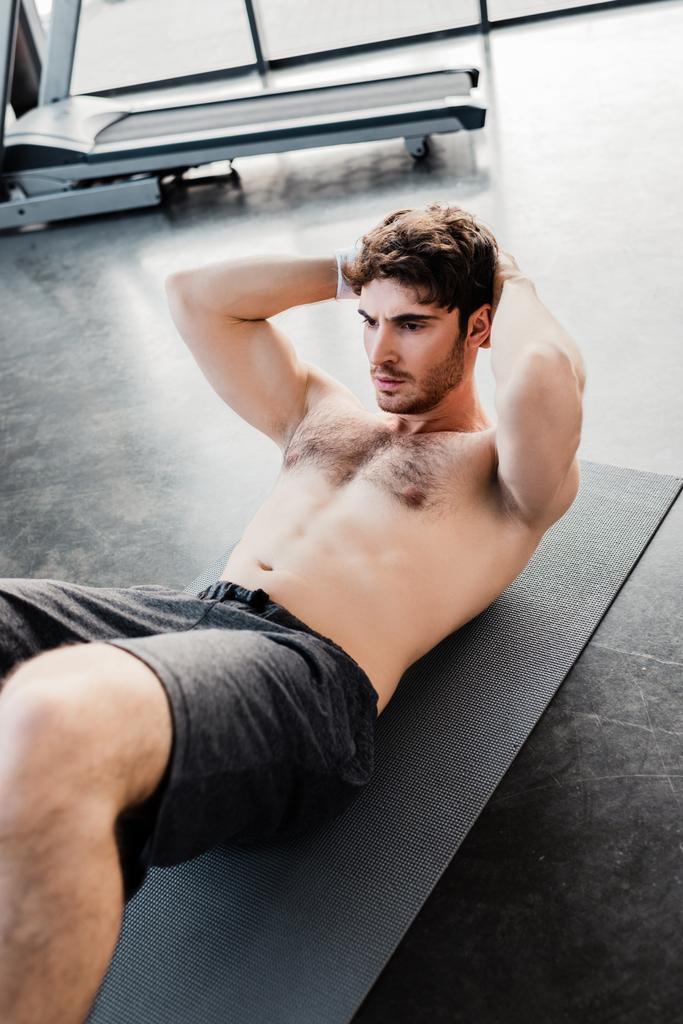 selective focus of muscular sportsman doing sit ups on fitness mat in gym  - Photo, Image