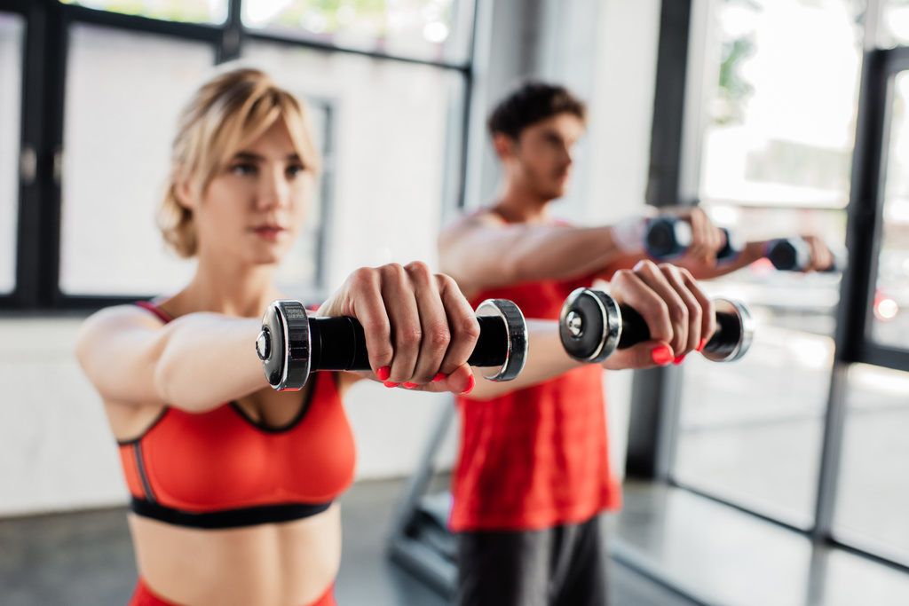 selective focus of young adult couple working out with dumbbells in gym  - Photo, Image