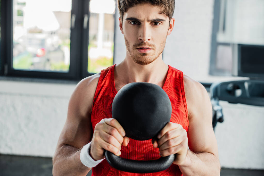 athletic man looking at camera and exercising with heavy dumbbell in sports center  - Photo, Image