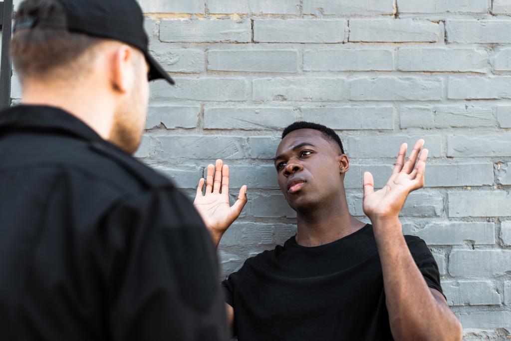 foco seletivo do homem americano africano com as mãos levantadas olhando para o policial, conceito de racismo
  - Foto, Imagem