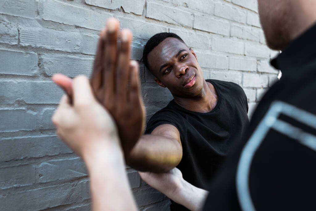 επιλεκτική εστίαση του τραυματισμένου Αφροαμερικανού άνδρα κοιτάζοντας αστυνομικός αγγίζοντας το χέρι, έννοια του ρατσισμού  - Φωτογραφία, εικόνα