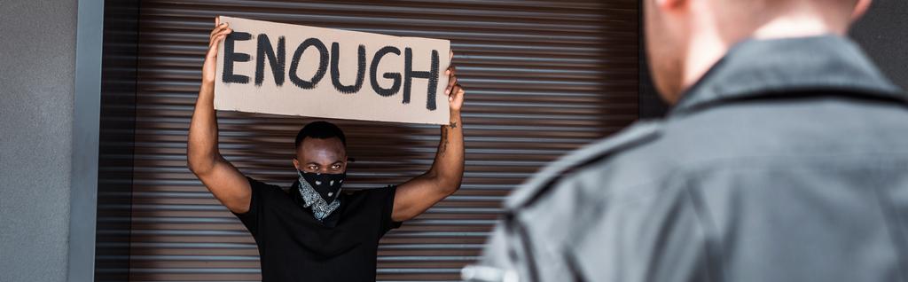 culture horizontale de l'homme afro-américain tenant une pancarte avec assez de lettrage près de policier, concept de racisme  - Photo, image