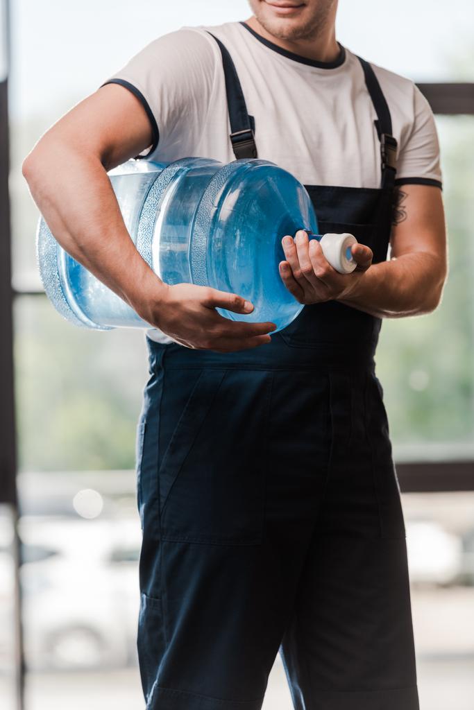 bijgesneden weergave van de levering man in uniform bedrijf flessenwater  - Foto, afbeelding