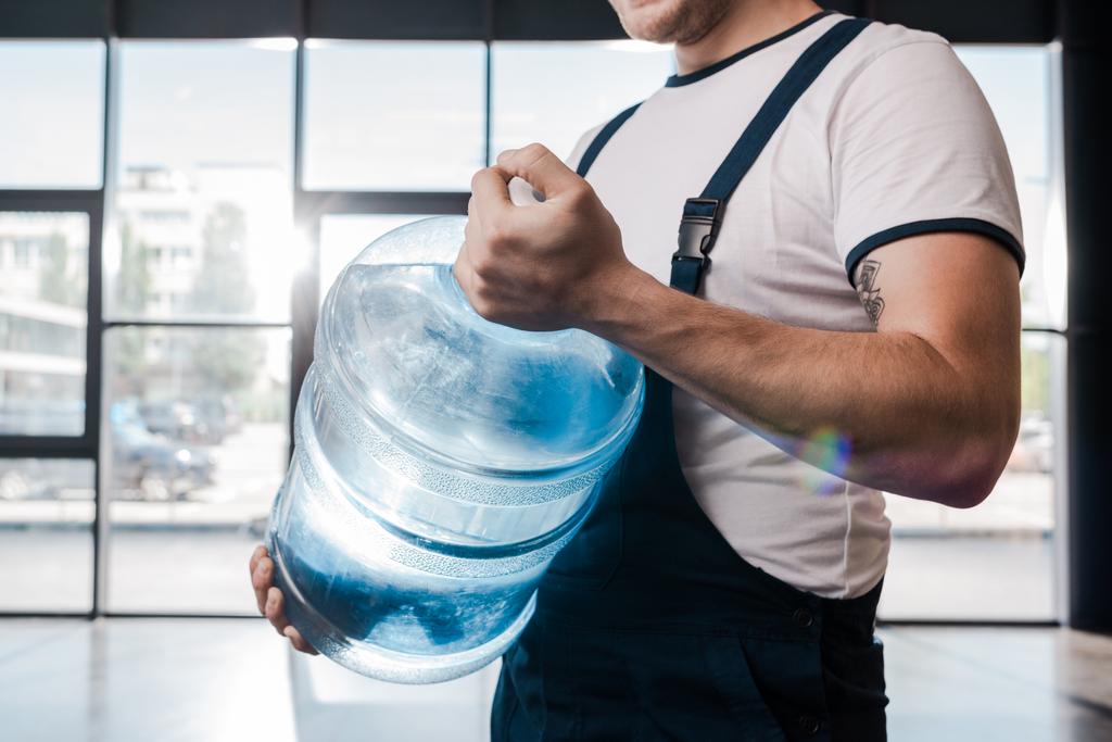 vista recortada del repartidor hombre sosteniendo pesado galón con agua
  - Foto, imagen