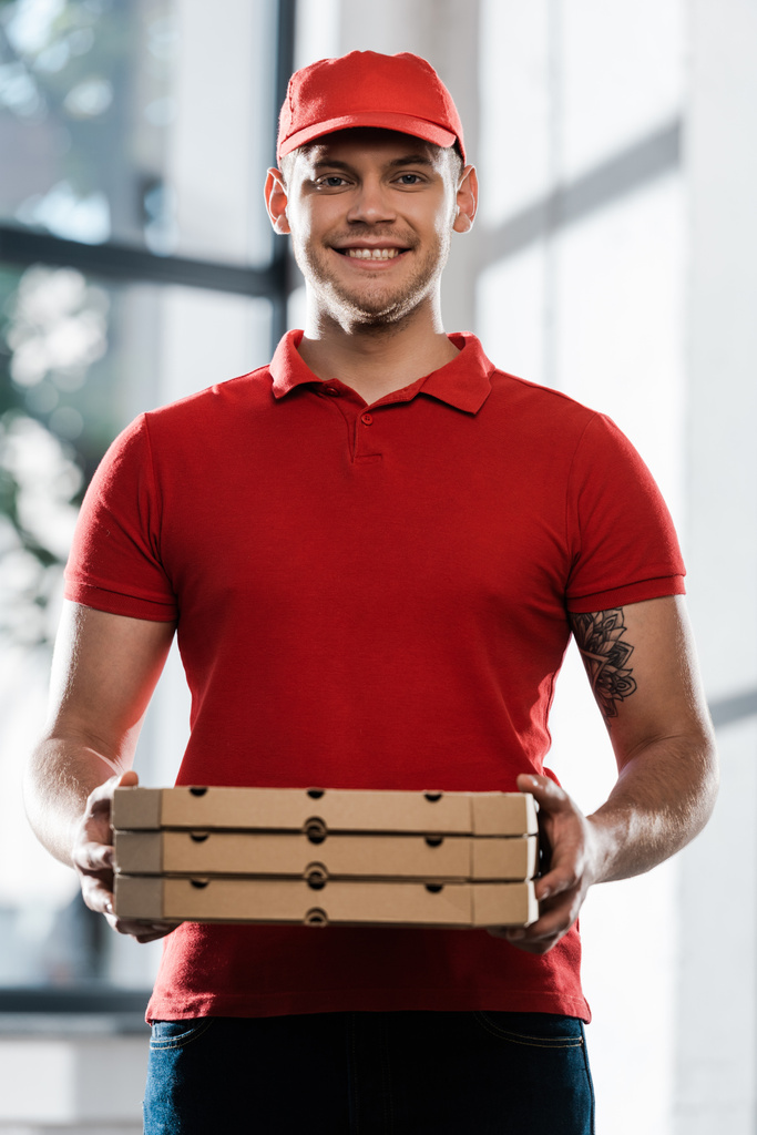 cheerful delivery man in cap and uniform holding pizza boxes  - Photo, Image
