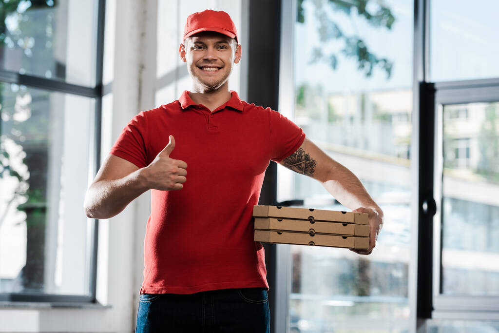 felice uomo di consegna mostrando pollice in su e tenendo scatole di pizza  - Foto, immagini