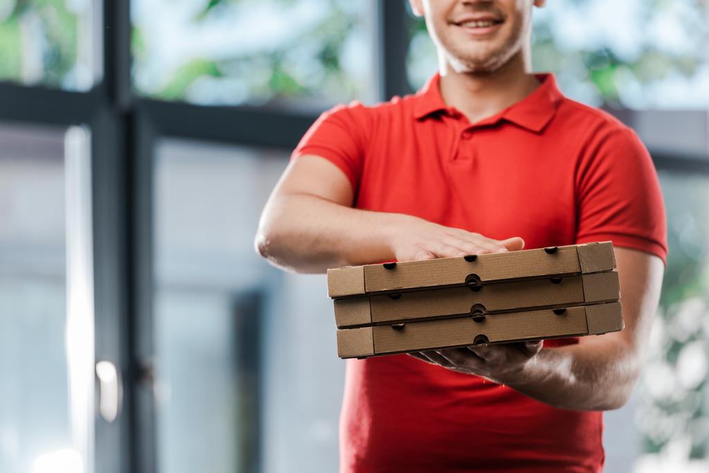 καλλιεργημένη άποψη του χαμογελαστού ντελιβερά κρατώντας κουτιά πίτσα  - Φωτογραφία, εικόνα