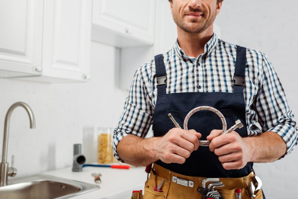 Ausgeschnittene Ansicht des Klempners in Arbeitskleidung und Werkzeuggürtel mit Metallrohr in der Küche  - Foto, Bild