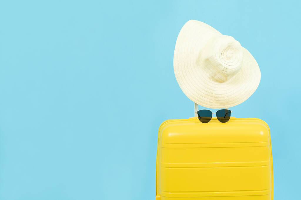 Летние каникулы, отдых и путешествия concept.Yellow Чемодан или багажная сумка с солнцезащитной шляпой на синем фоне для копирования пространства
. - Фото, изображение