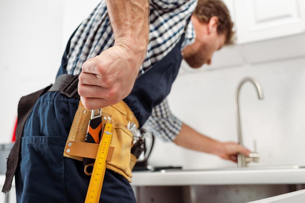 Selektiver Fokus des Klempners, der Schraubenschlüssel vom Werkzeugband nimmt, während er Wasserhahn in der Küche fixiert  - Foto, Bild