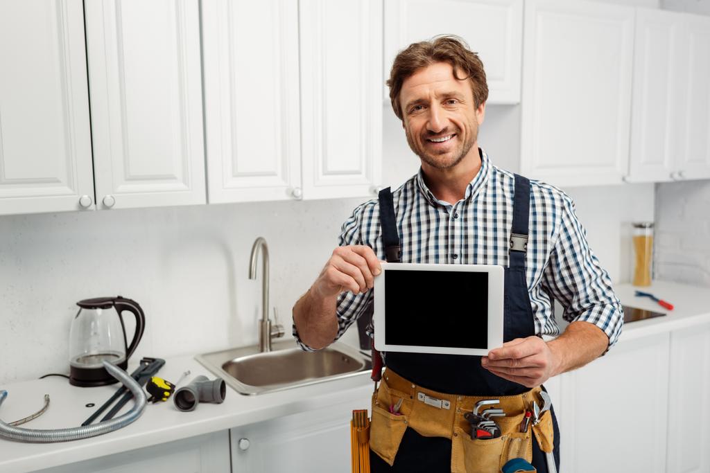 Trabajador sonriente sosteniendo tableta digital con pantalla en blanco cerca de herramientas en la encimera de la cocina
  - Foto, Imagen