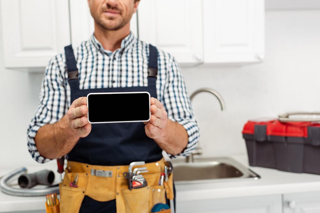 Vista ritagliata dello smartphone idraulico con schermo vuoto in cucina  - Foto, immagini