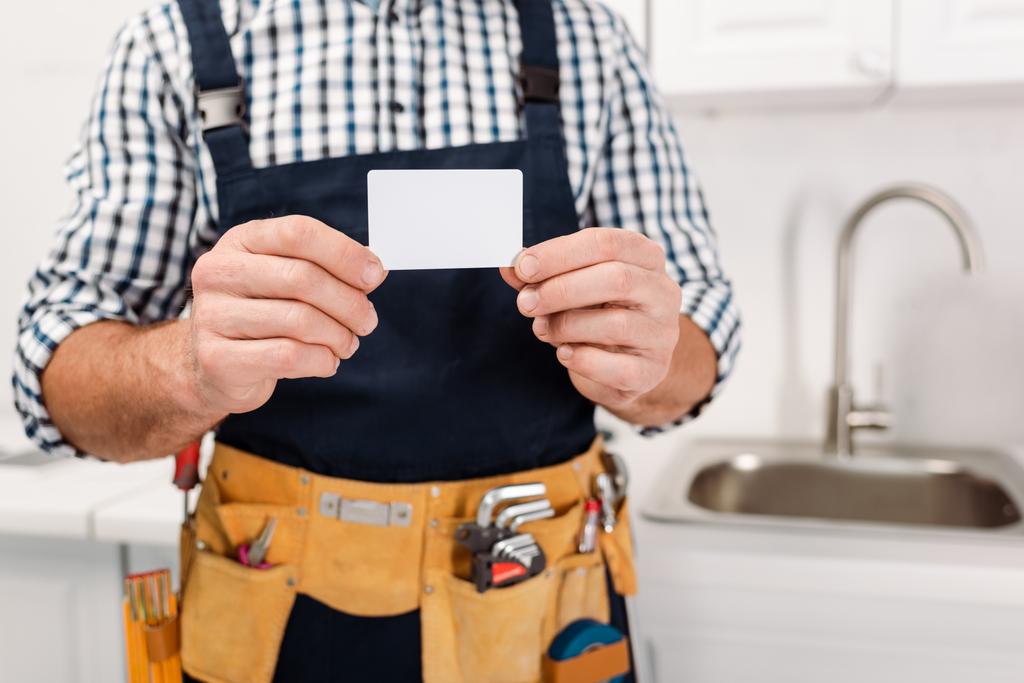 Oříznutý pohled na dělníka v opasku s nářadím s prázdnou kartou v kuchyni  - Fotografie, Obrázek
