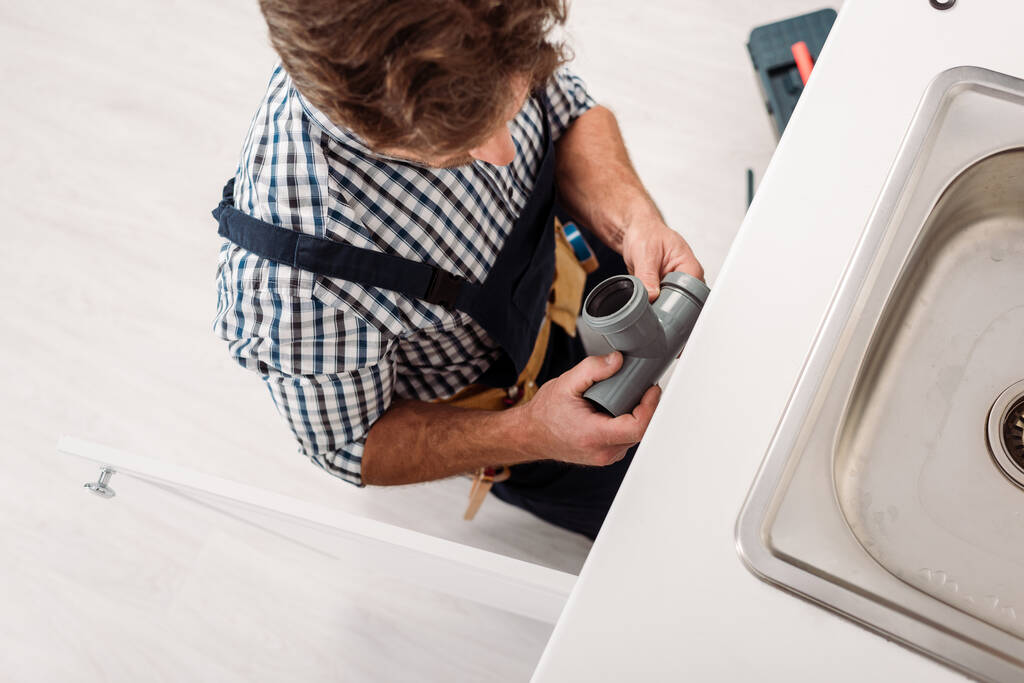 Felülnézet vízvezeték-szerelő tartja műanyag cső rögzítése közben mosogató a konyhában  - Fotó, kép