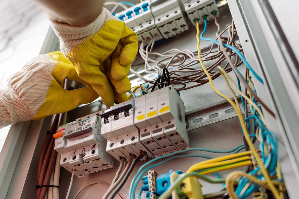 Vista de ángulo bajo del electricista en guantes que fijan la caja de distribución eléctrica
 - Foto, imagen