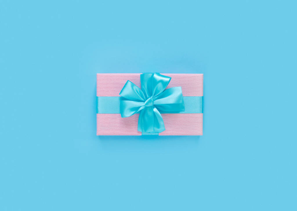 Ροζ κουτί δώρου με φιόγκο και κορδέλα σε μπλε χάρτινο φόντο με κενό χώρο για κείμενο. Αντιγραφή χώρου για κείμενο. Επίπεδη lay, κορυφαία άποψη έννοια. - Φωτογραφία, εικόνα