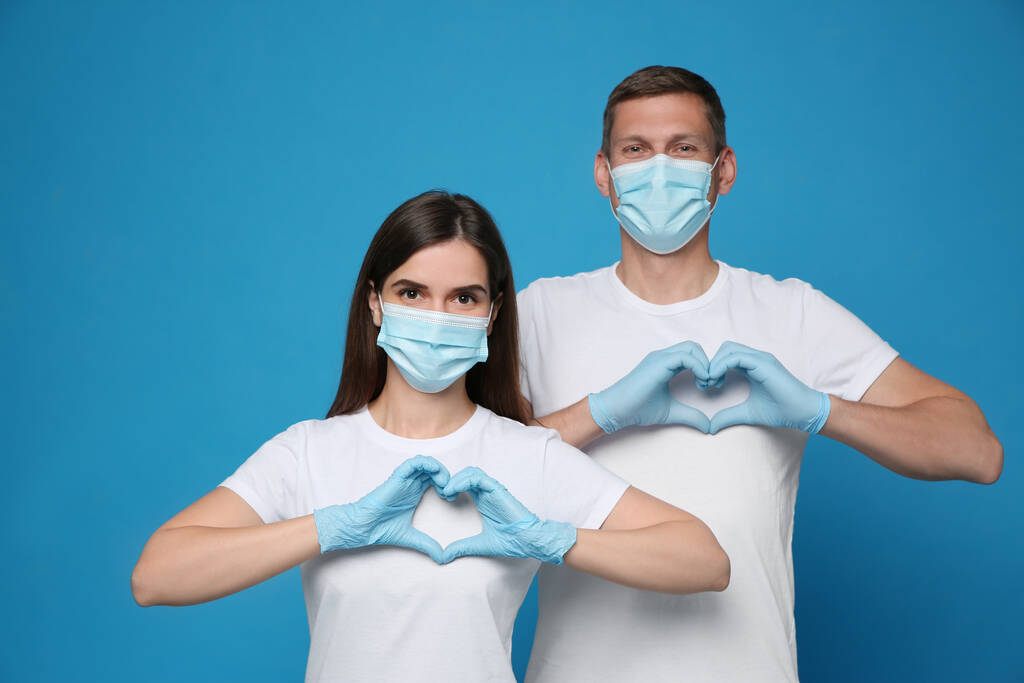 Dobrovolníci v ochranných maskách a rukavicích s gesty srdce na modrém pozadí. Podpora během karantény koronaviru - Fotografie, Obrázek