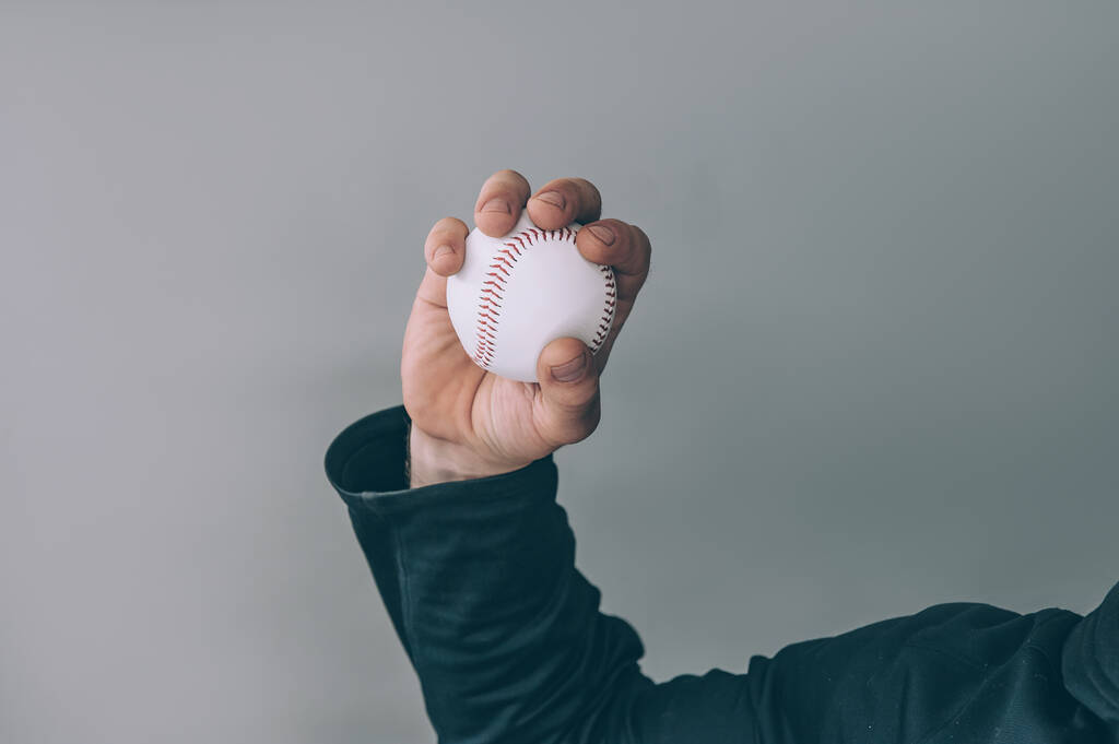 Le gars tient une balle de baseball dans sa main sur un fond gris - Photo, image
