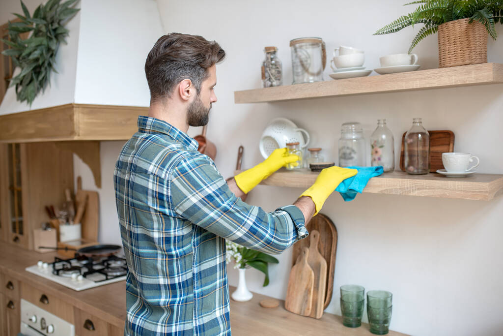 Mies keltaisissa hanskoissa puhdistamassa hyllyä keittiössä - Valokuva, kuva