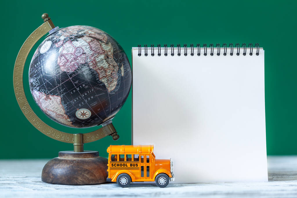 Terug naar school concept. Gele schoolbus speelgoed model en leeg blanco met wereldbol en schoolbenodigdheden - Foto, afbeelding