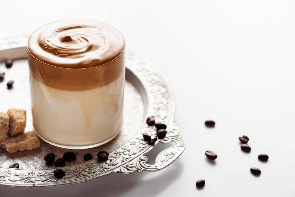 delicious Dalgona coffee in glass near coffee beans, brown sugar on silver platter on white background - Photo, Image