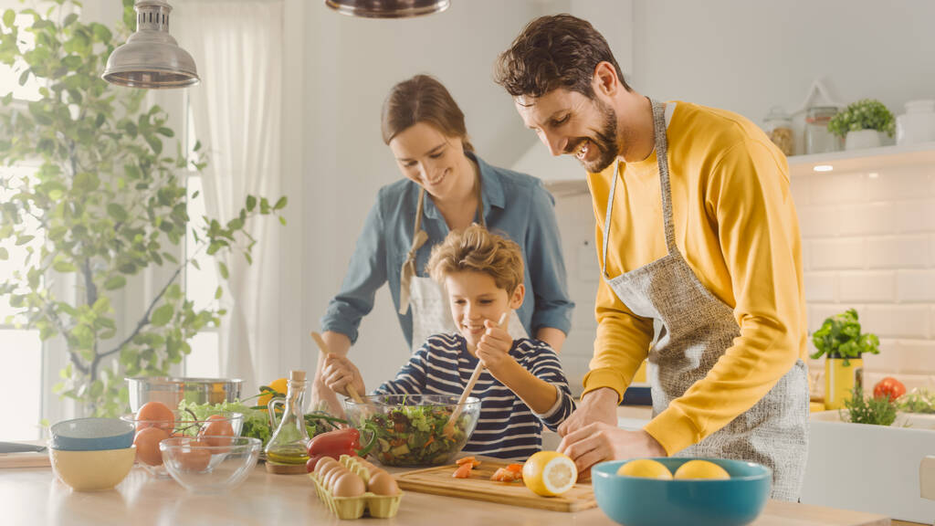 Mutfakta, Anne, Baba ve Şirin Çocuk Sağlıklı Yemek Yapıyor. Ebeveynler küçük oğluna sağlıklı alışkanlıkları ve sebzeleri salata kasesinde nasıl karıştıracağını öğretiyor. Sevimli Çocuk Ailesine Yardım Ediyor - Fotoğraf, Görsel