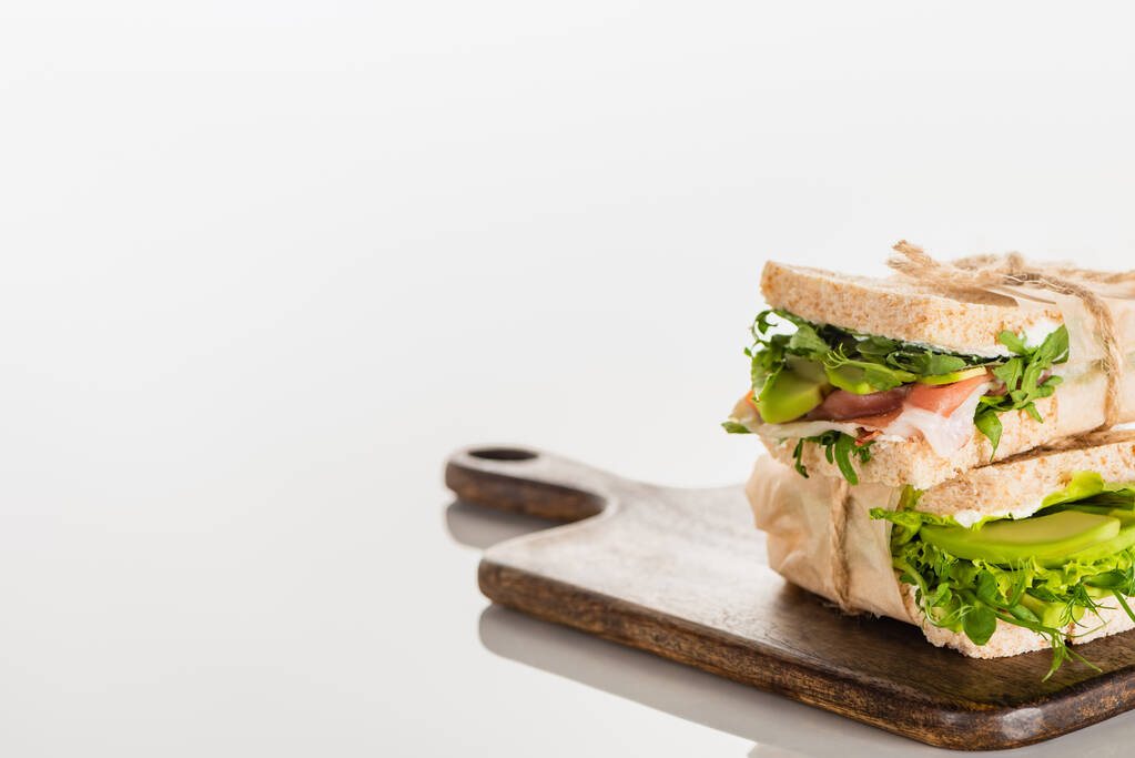selektivní zaměření čerstvých zelených sendvičů s avokádem a masem na dřevěné řezací desce na bílém povrchu - Fotografie, Obrázek
