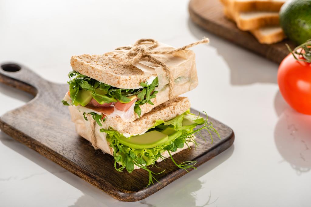 focus selettivo di panini verdi freschi con avocado e carne su tagliere in legno su superficie di marmo bianco - Foto, immagini