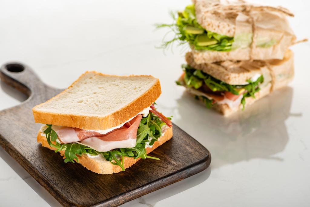 селективный фокус свежего зеленого сэндвича с прошутто на деревянной доске для резки белого мрамора
 - Фото, изображение