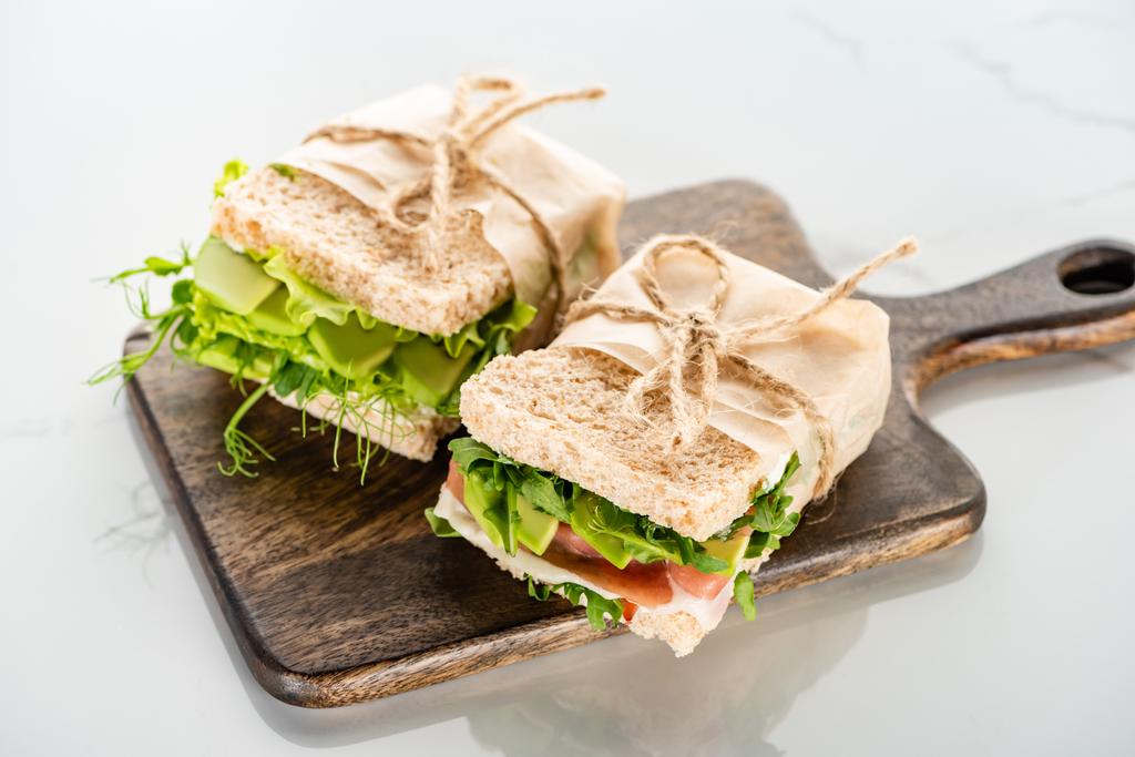 verse groene sandwiches met avocado en vlees op houten snijplank op wit oppervlak - Foto, afbeelding
