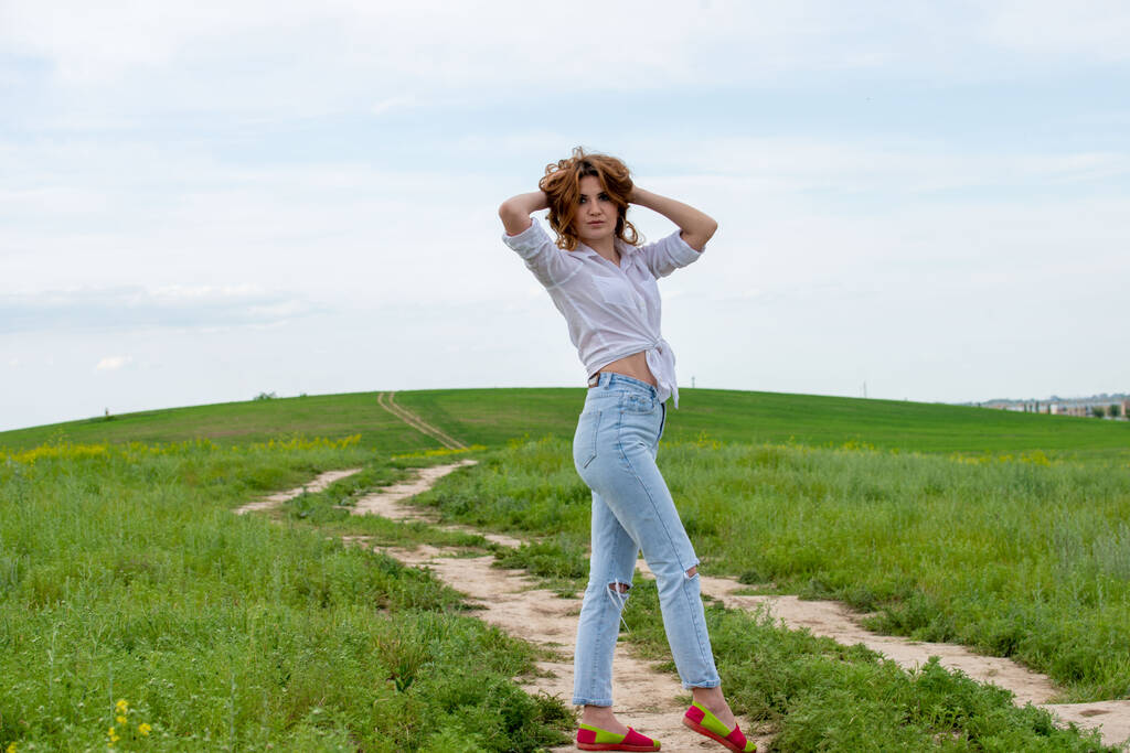 жінка в білій сорочці і блакитні джинси позує на полі
 - Фото, зображення