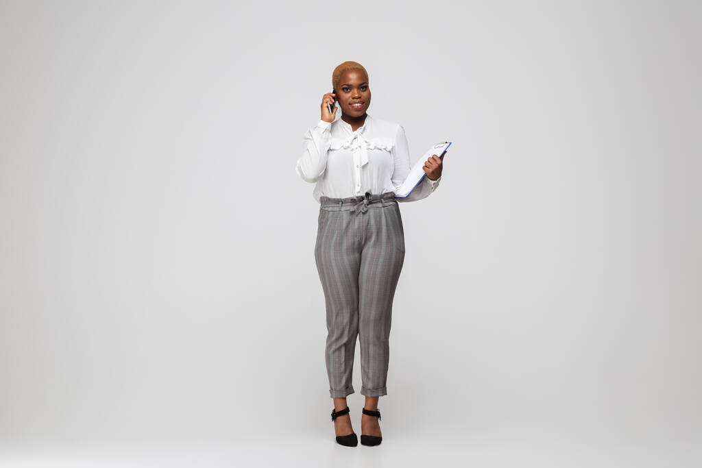 Jeune femme afro-américaine en tenue de bureau sur fond gris. Caractère féminin positif au corps. plus taille femme d'affaires - Photo, image