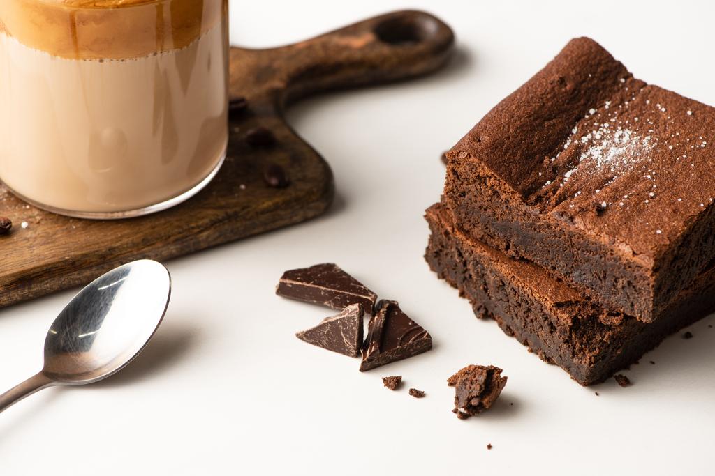 delicious brownie pieces near wooden cutting board with coffee and spoon on white background - Photo, Image
