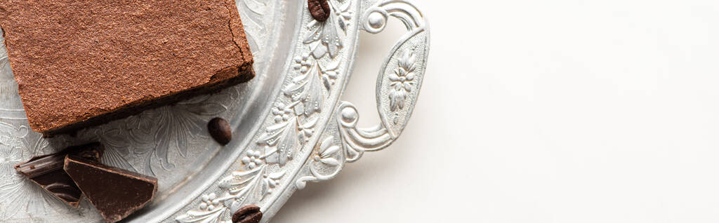bovenaanzicht van heerlijke brownie stuk met koffiebonen en chocolade op zilveren dienblad op witte achtergrond, panoramisch schot - Foto, afbeelding