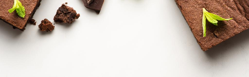 bovenaanzicht van heerlijke brownie stukken met munt op witte achtergrond, panoramisch schot - Foto, afbeelding