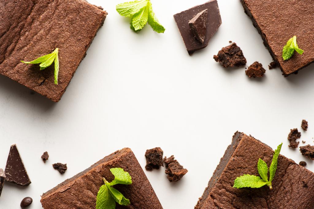 bovenaanzicht van heerlijke brownie stukjes met munt en chocolade op witte achtergrond - Foto, afbeelding