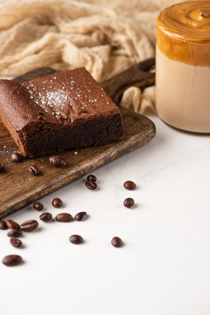 delicious brownie piece on wooden cutting board with coffee beans, coffee and cloth on white background - Photo, Image