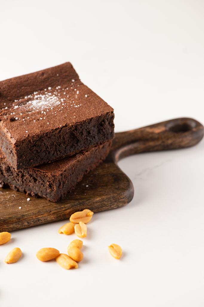 deliciosas piezas de brownie en tabla de cortar de madera con cacahuetes sobre fondo blanco
 - Foto, Imagen