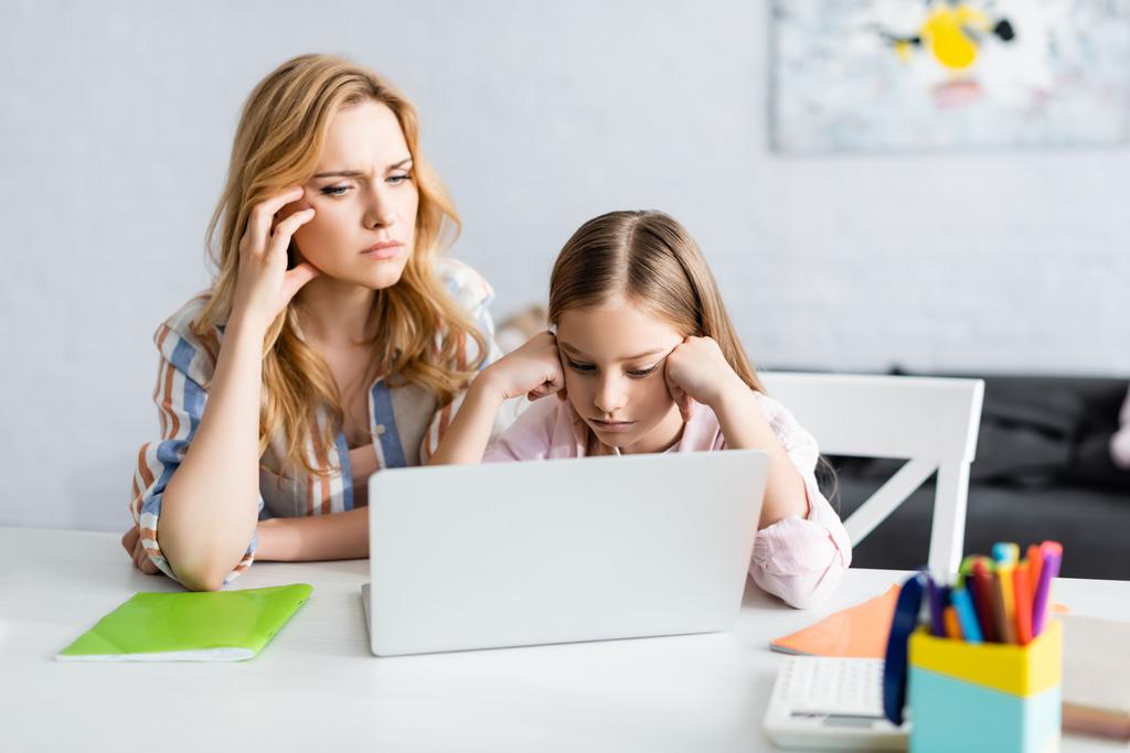 Enfoque selectivo de la madre pensativa y el niño mirando a la computadora portátil durante la educación en línea en el hogar
  - Foto, Imagen