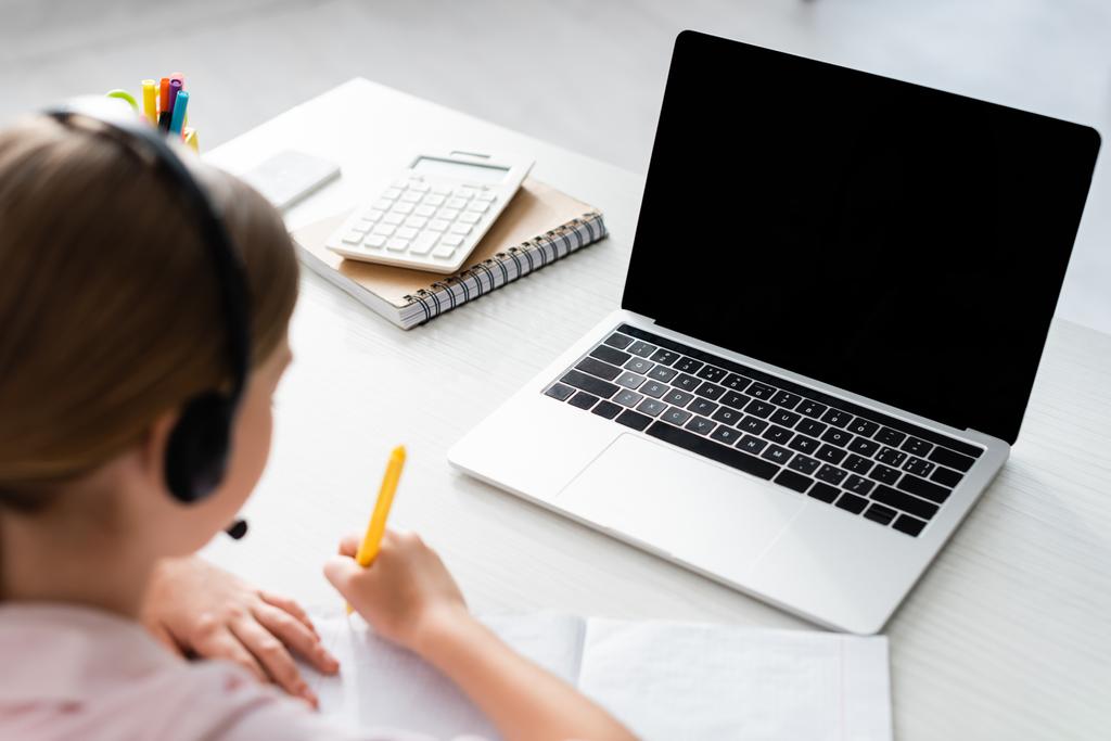 Селективное внимание ребенка в гарнитуре записи на ноутбуке рядом с ноутбуком и канцелярские принадлежности на столе
  - Фото, изображение